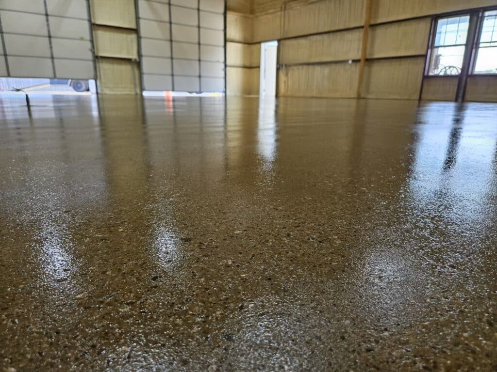 This is a low-angle view of a shiny concrete floor inside a spacious industrial hangar with metallic walls and a window allowing daylight in.