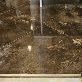 This image showcases a section of glossy, brown-tiled floor with visible reflective streaks and marks. There's a metal door threshold leading to another area.