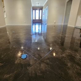 A spacious room with shiny polished concrete floors and walls painted in a light neutral color. Sunlight streams in from the doorway at the end.