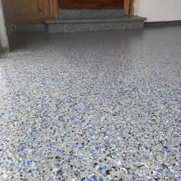 This image shows a speckled epoxy floor with shades of blue, gray, and white. In the background, there's a wooden door and part of a bare wall.